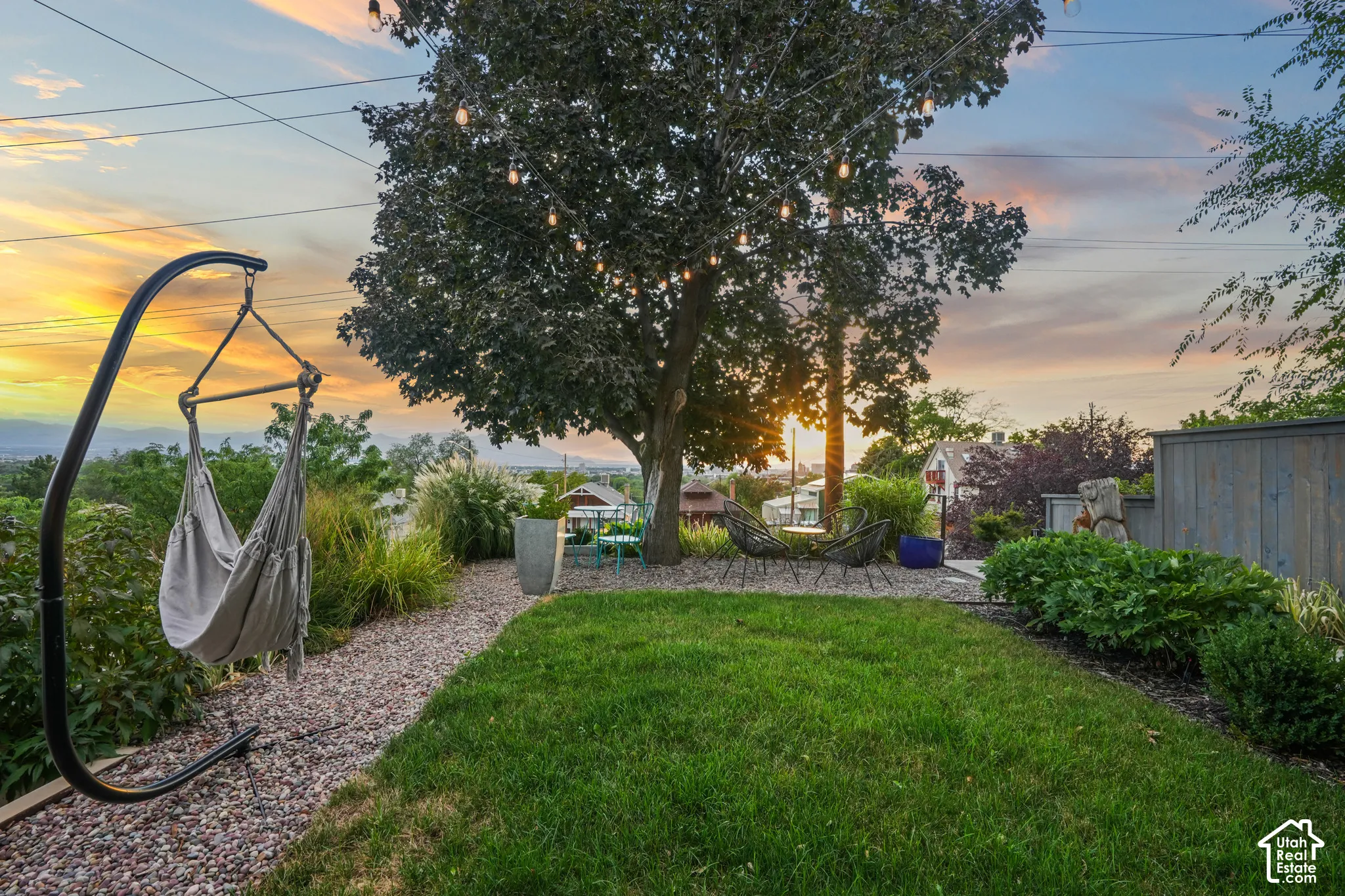 Manicured lawn with a gravel pathway, mature shade tree with string lighting, and established perimeter landscaping