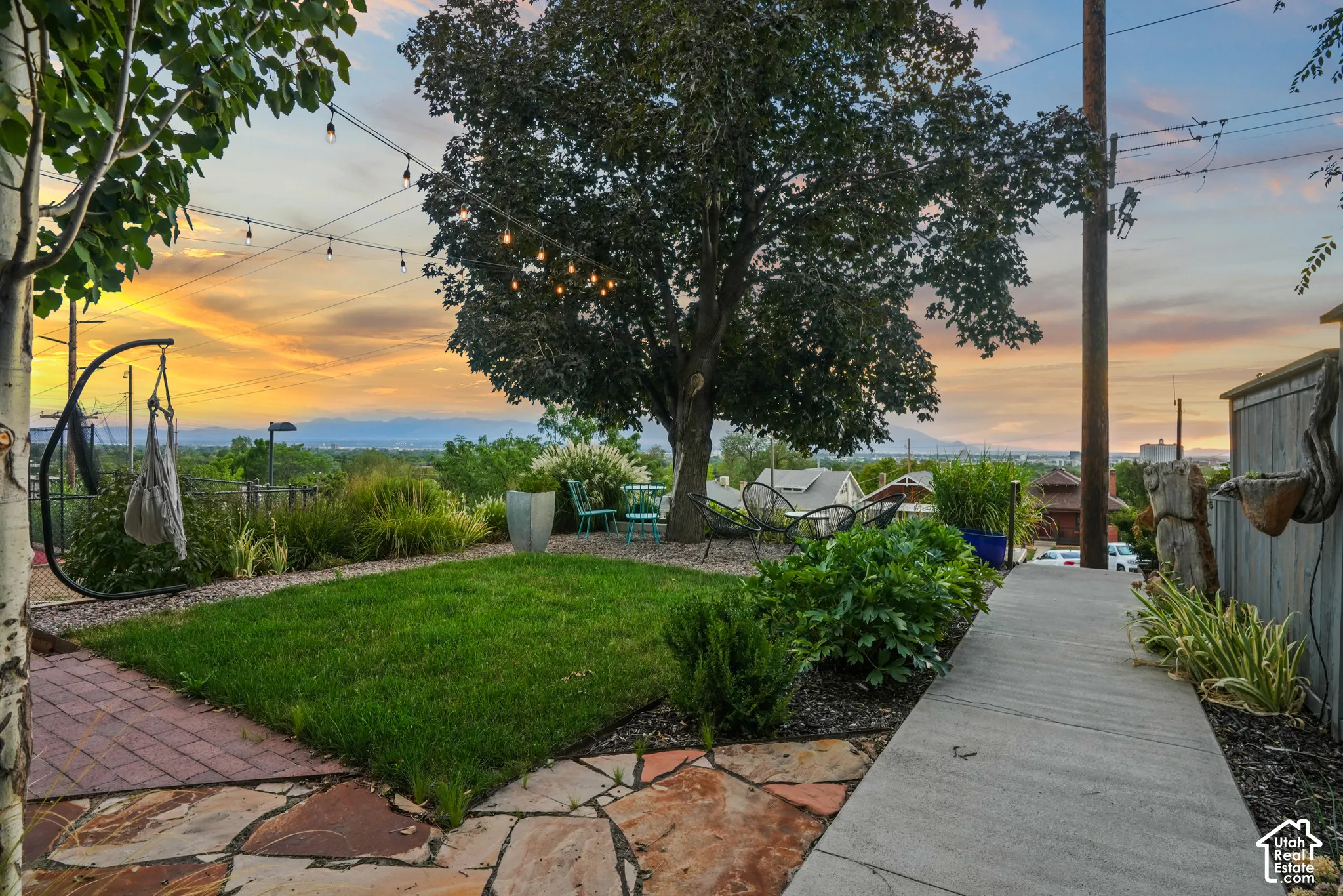Expansive backyard featuring a manicured lawn, flagstone patio, concrete pathway, and mature trees