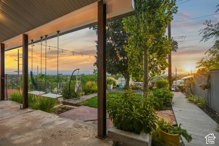 Covered patio with concrete flooring, mature landscaping, and a paved pathway