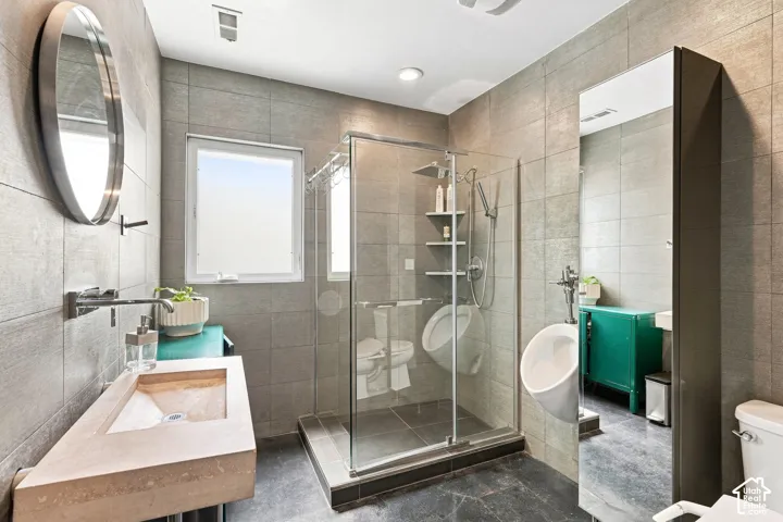 Slab vanity with an integrated sink and wall-mounted faucet, glass-enclosed shower, and tiled walls and flooring
