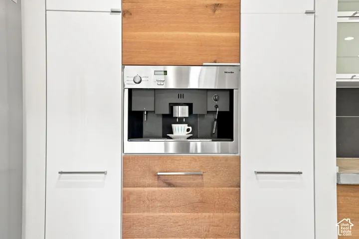 Built-in stainless steel coffee system integrated into custom cabinetry, featuring white flat-panel doors and wood-finish accents