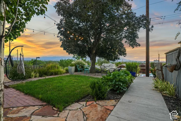 Expansive backyard featuring a manicured lawn, flagstone patio, concrete pathway, and mature trees