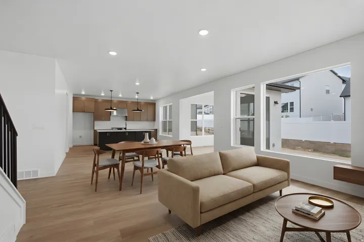 Open-concept living space featuring hardwood flooring throughout, a tan upholstered sofa, and abundant natural light from expansive glass doors and windows
