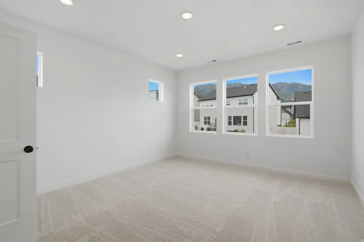 Bright, light-filled bedroom with triple windows framing mountain scenery, recessed ceiling lighting, neutral wood-finish flooring, and fresh white wall finishes