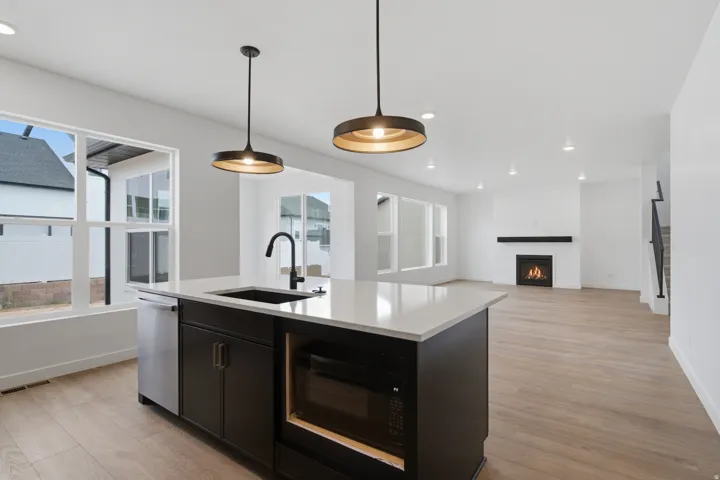 Modern kitchen and great room featuring a black cabinetry island with white quartz countertop, stainless steel appliances, and matte black faucet