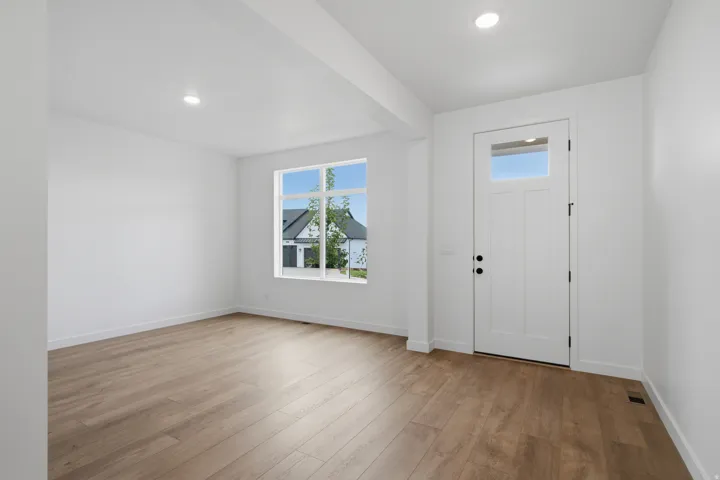 Bright, open living space featuring gleaming wood-finish flooring, recessed ceiling lighting, and abundant natural light from a large picture window