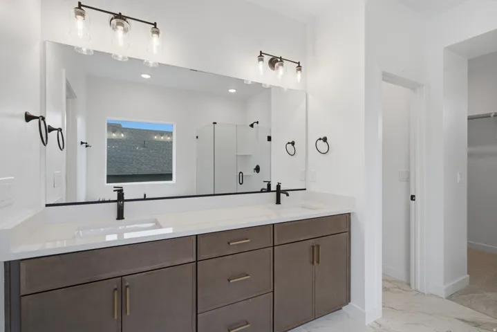 Spa-inspired primary bathroom featuring a dual-sink vanity with wood-finish cabinetry, white quartz countertops, and matte black hardware