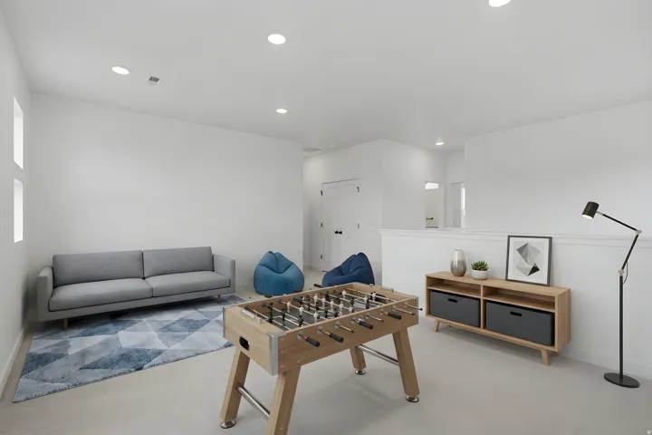 Modern recreational space featuring recessed ceiling lighting, a wood-finish foosball table, neutral wall-to-wall flooring, built-in cabinetry with integrated storage, and a contemporary gray upholstered sofa
