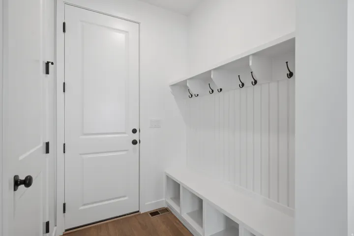 Bright, organized entryway featuring white shaker-style paneling, built-in cubbies with storage shelving, and a wall-mounted coat rack with multiple hooks