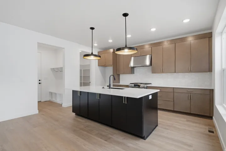 Contemporary kitchen featuring natural wood-finish cabinetry, a contrasting black center island with white quartz countertop, stainless steel appliances, subway tile backsplash, and pendant lighting