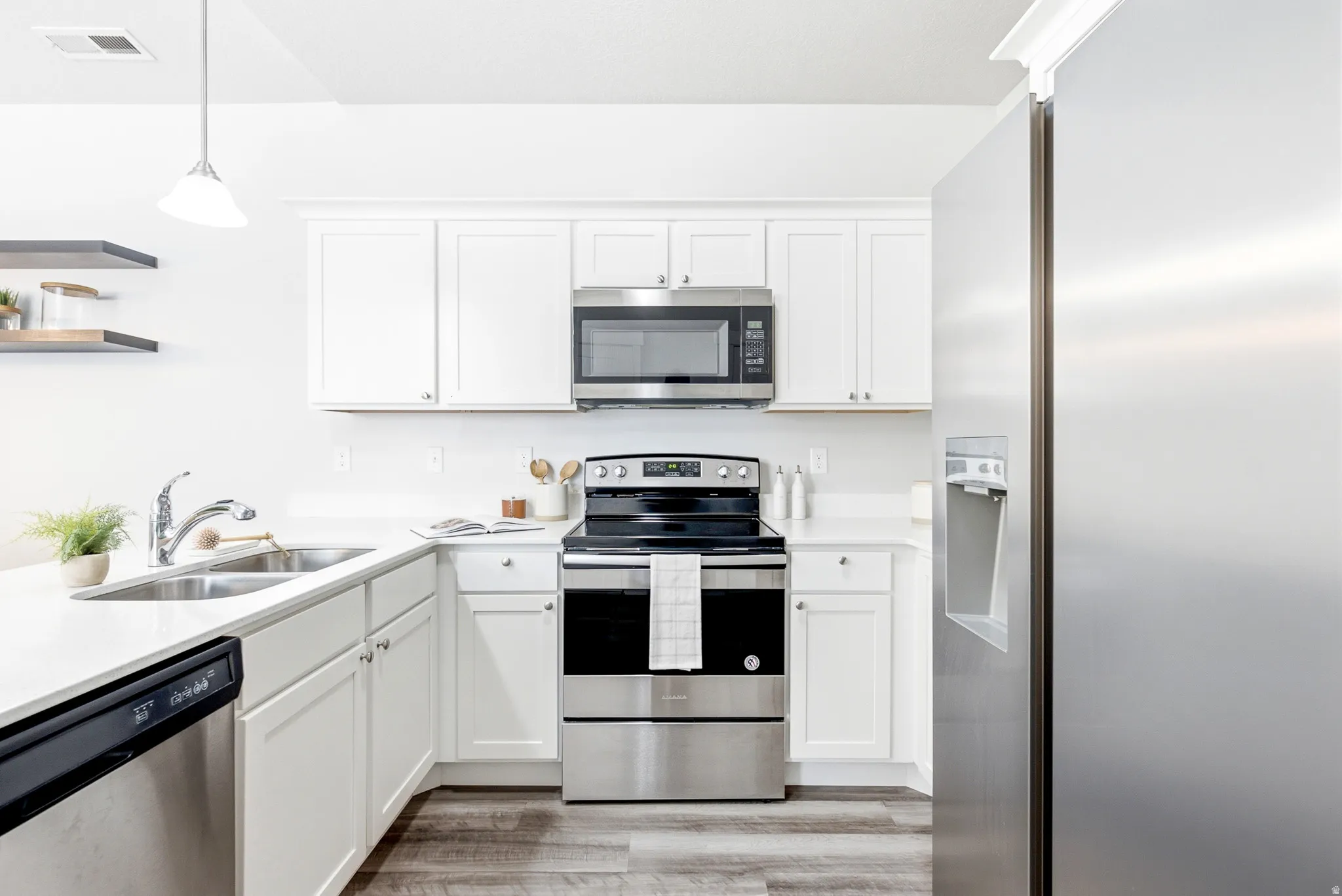 Modern kitchen featuring stainless steel appliances including a gas range with dual ovens, over-the-range microwave, and refrigerator with ice and water dispenser