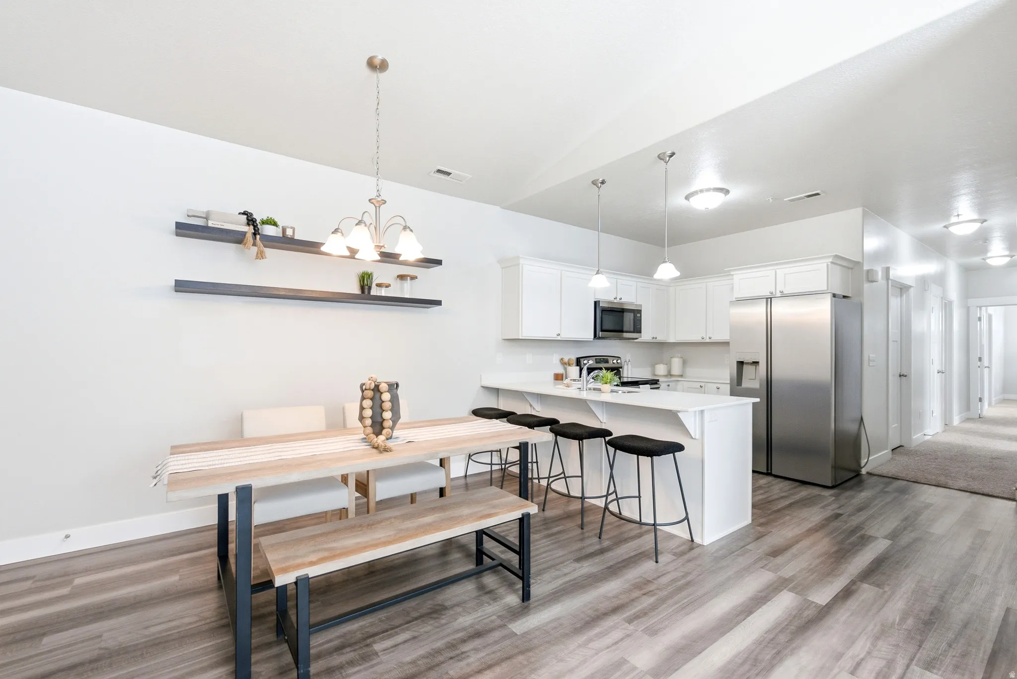 Open-concept kitchen and dining area featuring stainless steel appliances, white cabinetry, quartz countertops, wood-finish flooring, and a dining table with built-in bench seating