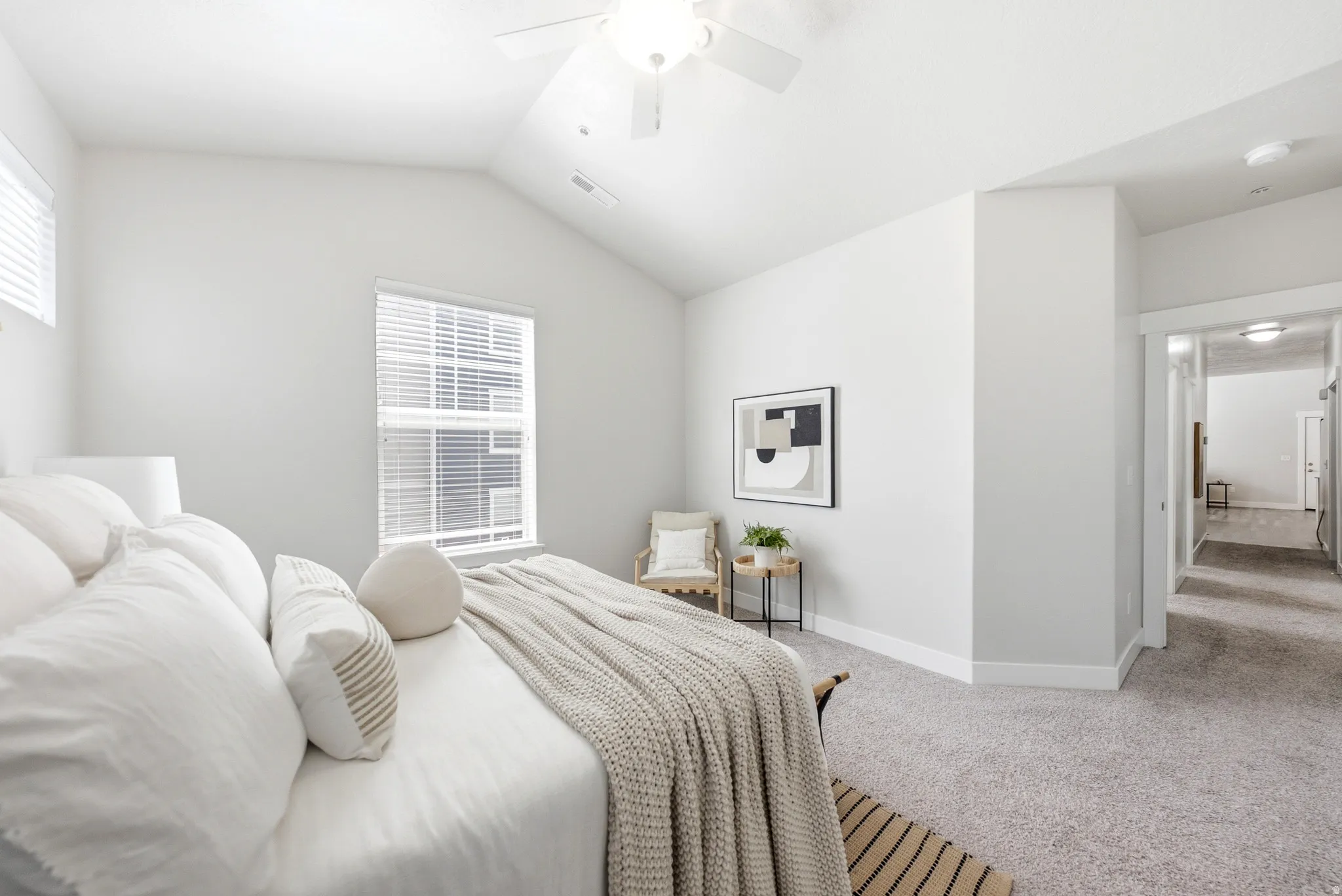 Bright primary bedroom featuring vaulted ceilings with ceiling fan, expansive windows with plantation shutters, neutral wall finishes, and direct access to ensuite bathroom