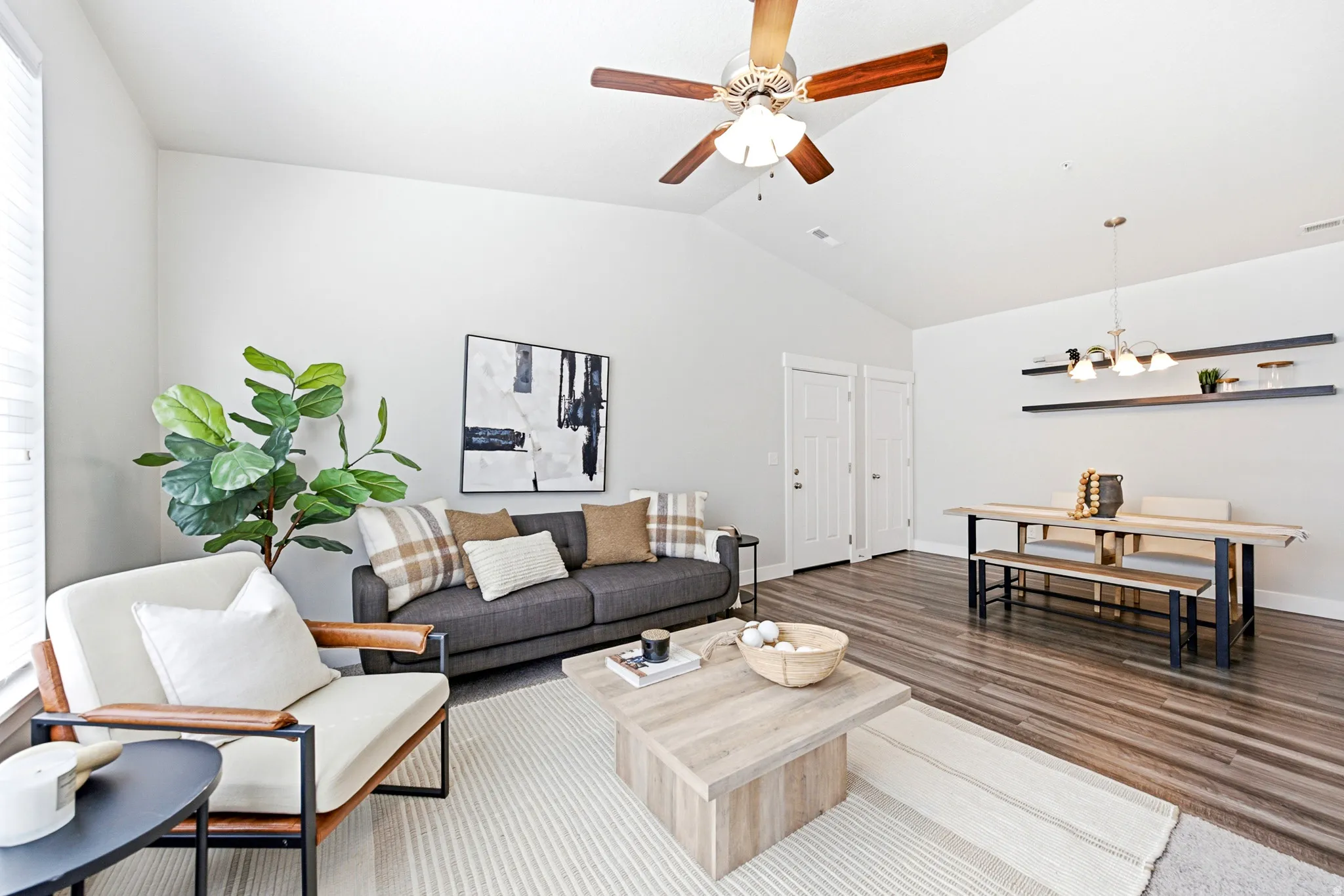 Open-concept living area featuring wood-finish flooring, a ceiling fan with integrated lighting, and abundant natural light