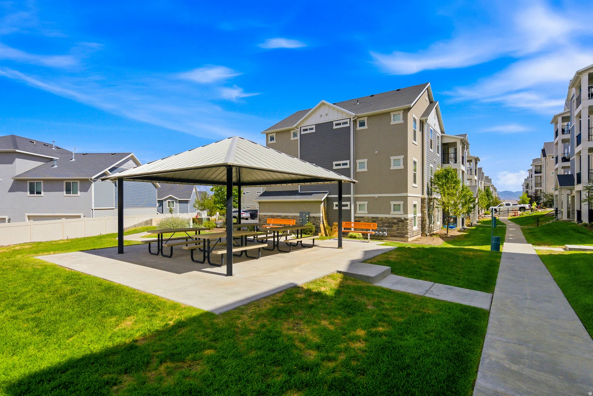 Expansive outdoor entertaining space featuring a modern shade structure with integrated seating area, concrete patio, and manicured lawn