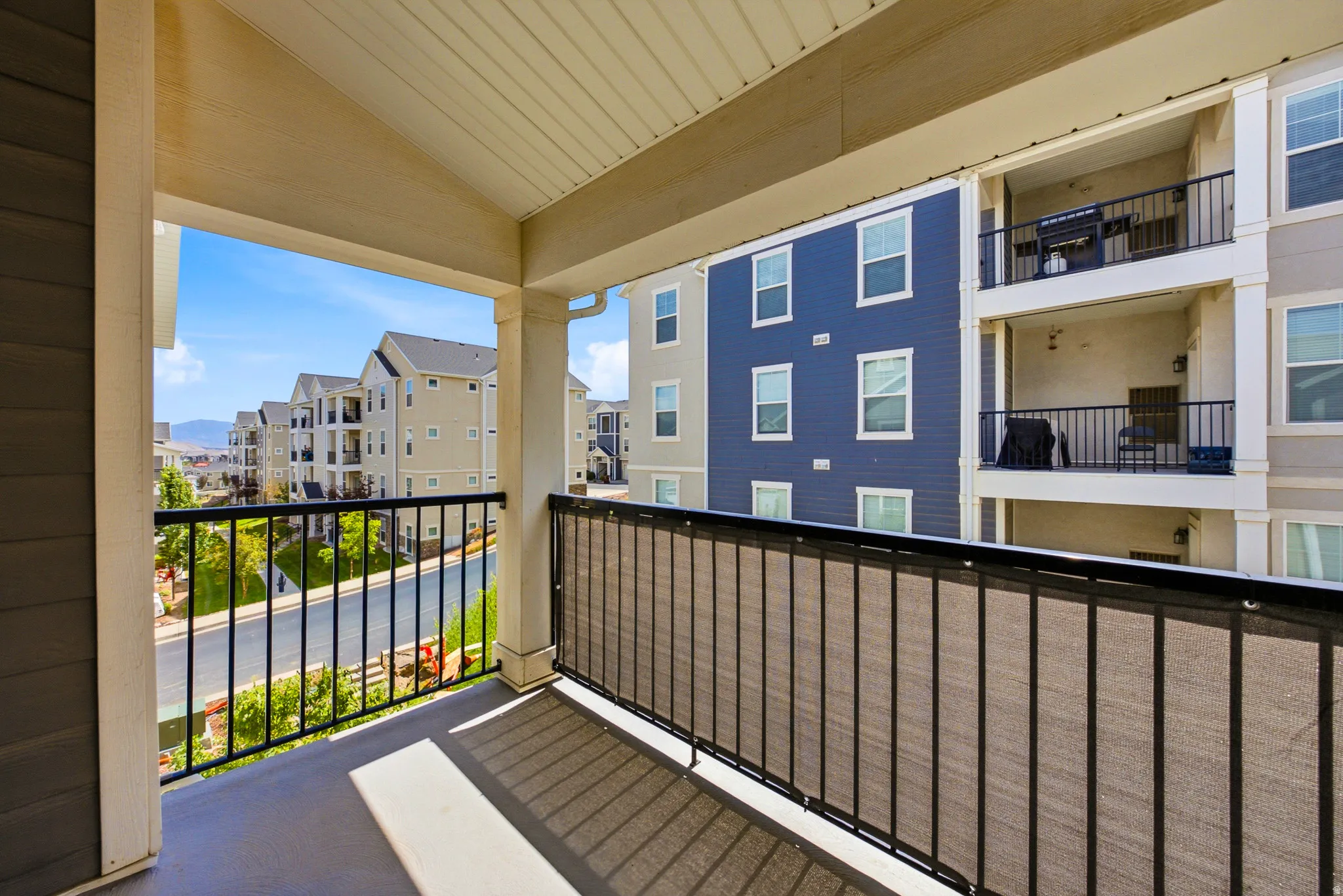 Covered balcony with composite decking and black metal railing, offering views of the surrounding residential community