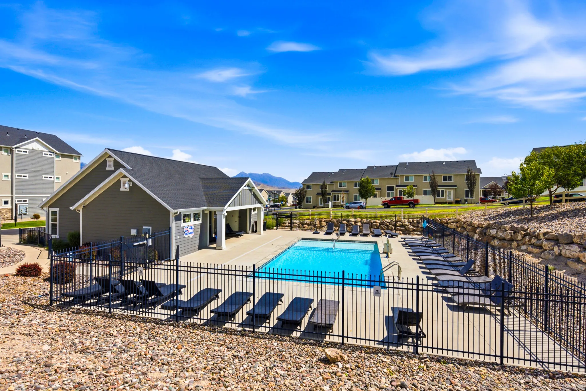 Resort-style community pool with crystal-blue water, surrounded by black metal fencing and lounge seating