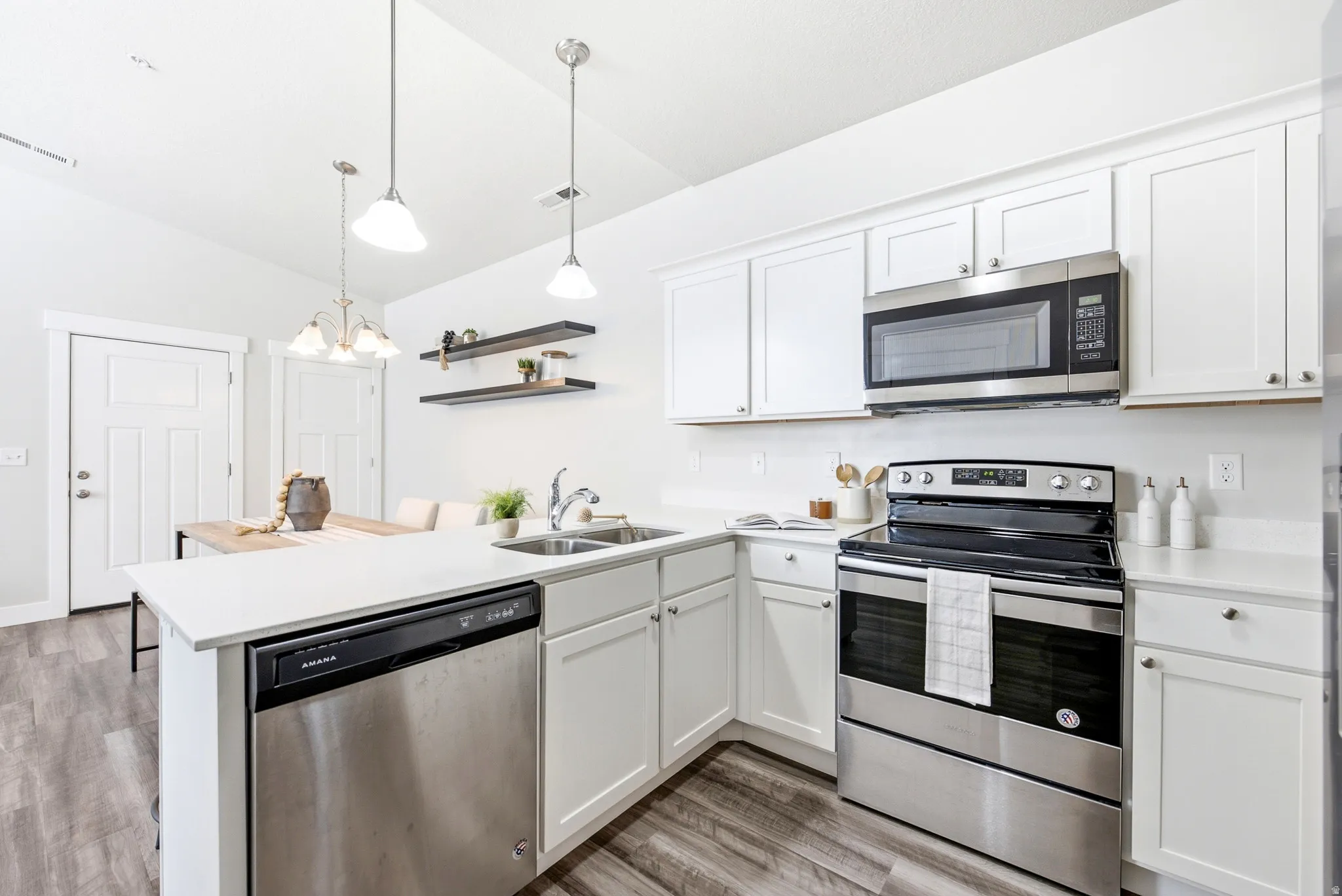 Modern kitchen featuring white cabinetry, stainless steel appliances including a dual-fuel range and over-the-range microwave, white subway tile backsplash, quartz countertops, a centered island with prep space, pendant lighting, and wood-finish flooring