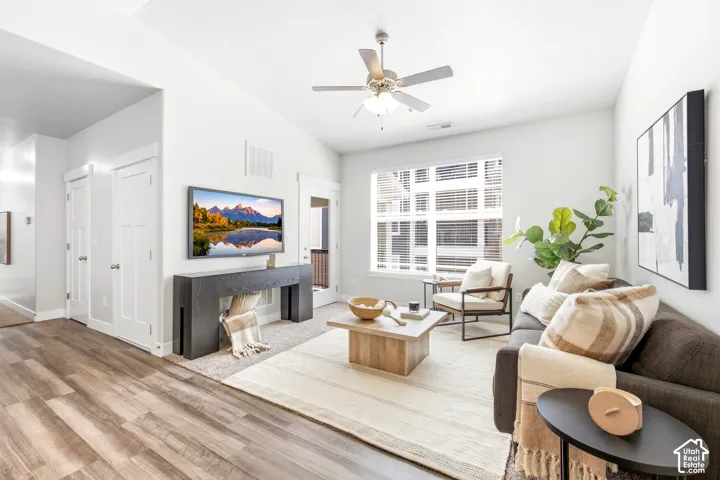 Bright, open living space showcasing wood-finish flooring, a ceiling fan with integrated lighting, and large multi-pane windows allowing natural light throughout