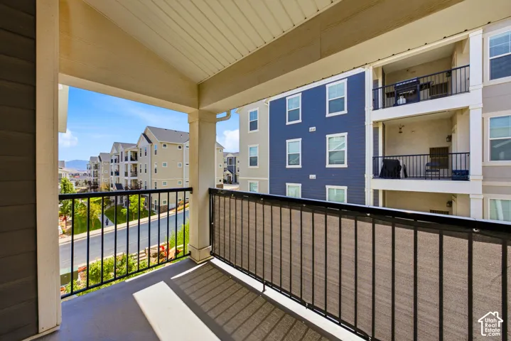 Covered balcony with composite decking and black metal railing, offering views of the surrounding residential community