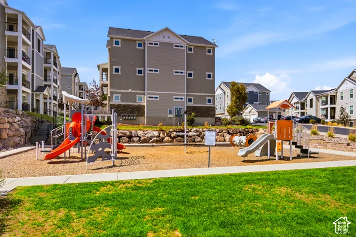 Community playground featuring dual slide structures, sandbox with natural wood edging, and manicured lawn with mature landscaping
