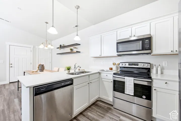 Modern kitchen featuring white cabinetry, stainless steel appliances including a dual-fuel range and over-the-range microwave, white subway tile backsplash, quartz countertops, a centered island with prep space, pendant lighting, and wood-finish flooring