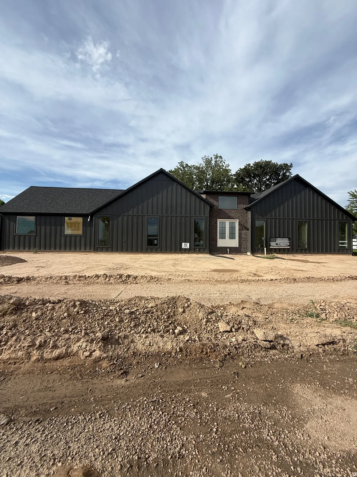 Modern exterior featuring dark vertical siding, white double doors, multiple large windows, and a dark shingle roof
