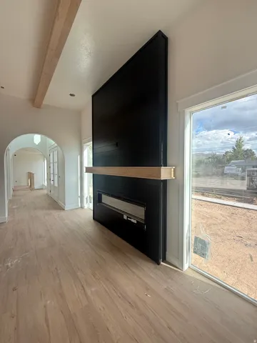 Wood-finish flooring, a black shiplap fireplace with a wood mantel, a linear electric fireplace, an arched entryway, and a wood ceiling beam