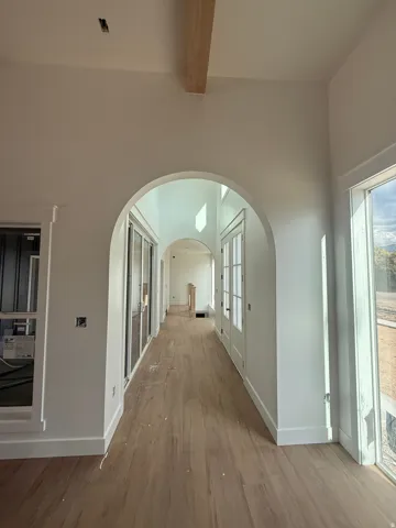 Arched entryway with a wood-finish flooring, high ceilings, and a wood beam accent