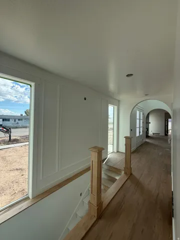 Expansive windows, board and batten wall detailing, wood-finish flooring, staircase with natural wood newel posts, and an arched hallway entry