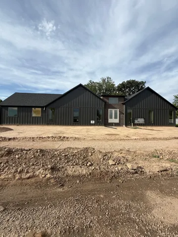 Modern exterior featuring dark vertical siding, white double doors, multiple large windows, and a dark shingle roof