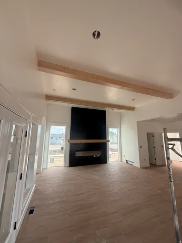 Spacious living area featuring a central fireplace with a wood mantel, exposed ceiling beams, and wood-finish flooring