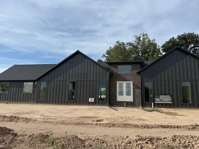Modern farmhouse design featuring a striking black metal exterior with multiple gabled rooflines, expansive glass windows and doors, and a central brick chimney detail