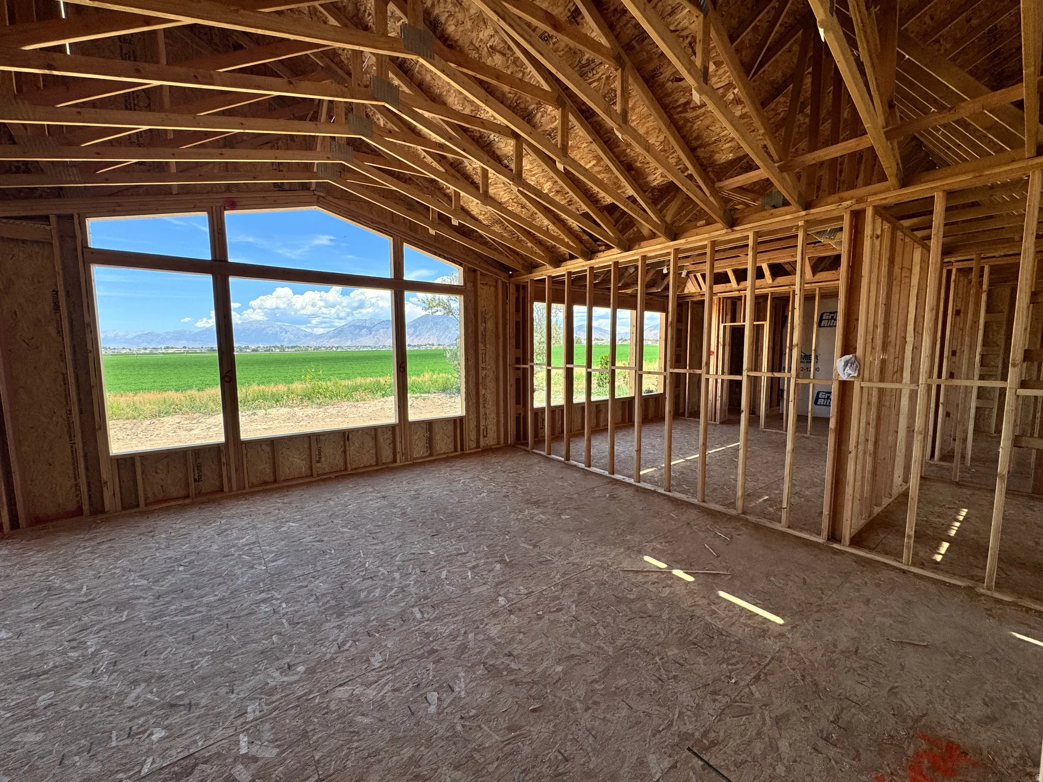 Spacious interior framed by expansive windows overlooking pastoral landscape, featuring exposed wood beam ceiling structure, concrete flooring, and wood-framed partition walls with metal studs ready for customization