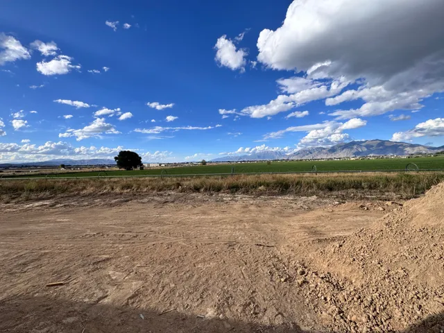 Expansive land parcel featuring a clear building area, surrounding green fields, and distant mountain ranges