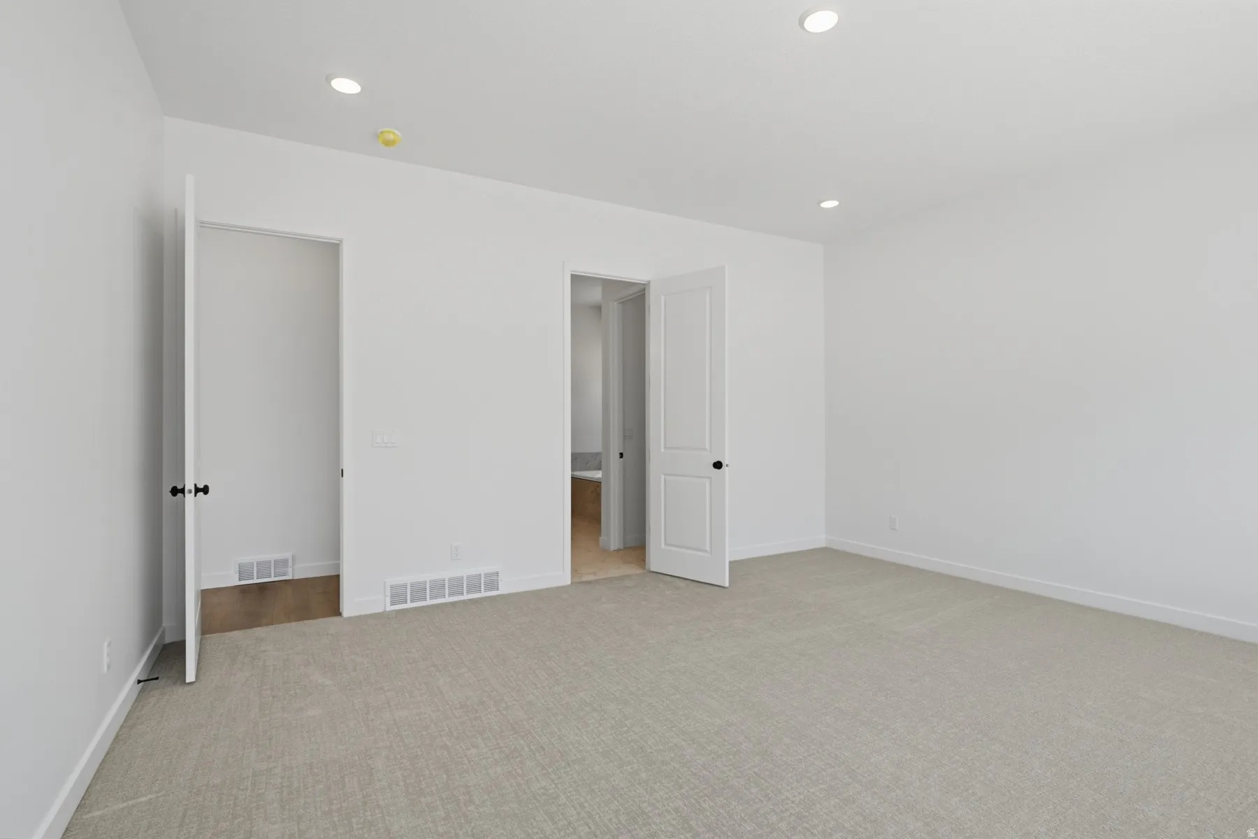 Light-toned carpeting, white walls, recessed ceiling lights, and two panel doors with dark hardware