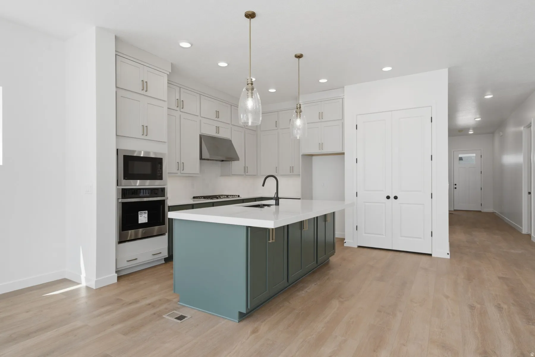 Kitchen featuring light-toned cabinetry, a contrasting island with a white countertop, stainless steel appliances, and wood-finish flooring