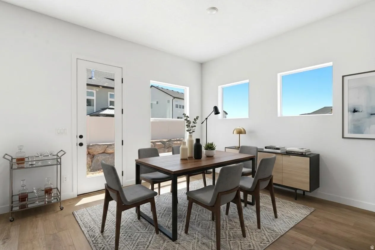 Contemporary dining space featuring a wood-finish table with metal frame seating for four, wide-plank wood flooring, and abundant natural light from multiple windows