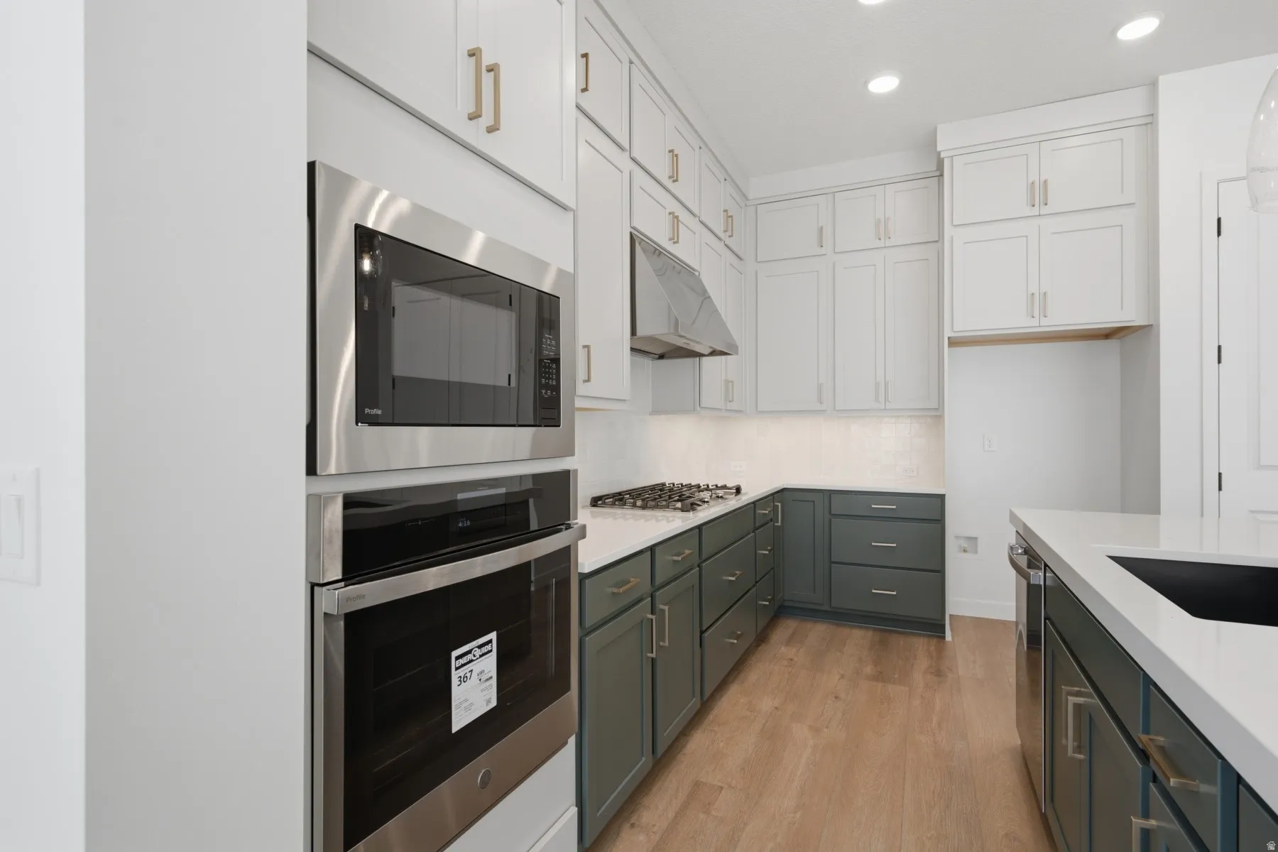 Modern kitchen featuring two-tone cabinetry, stainless steel appliances, a gas cooktop, and light wood-finish flooring