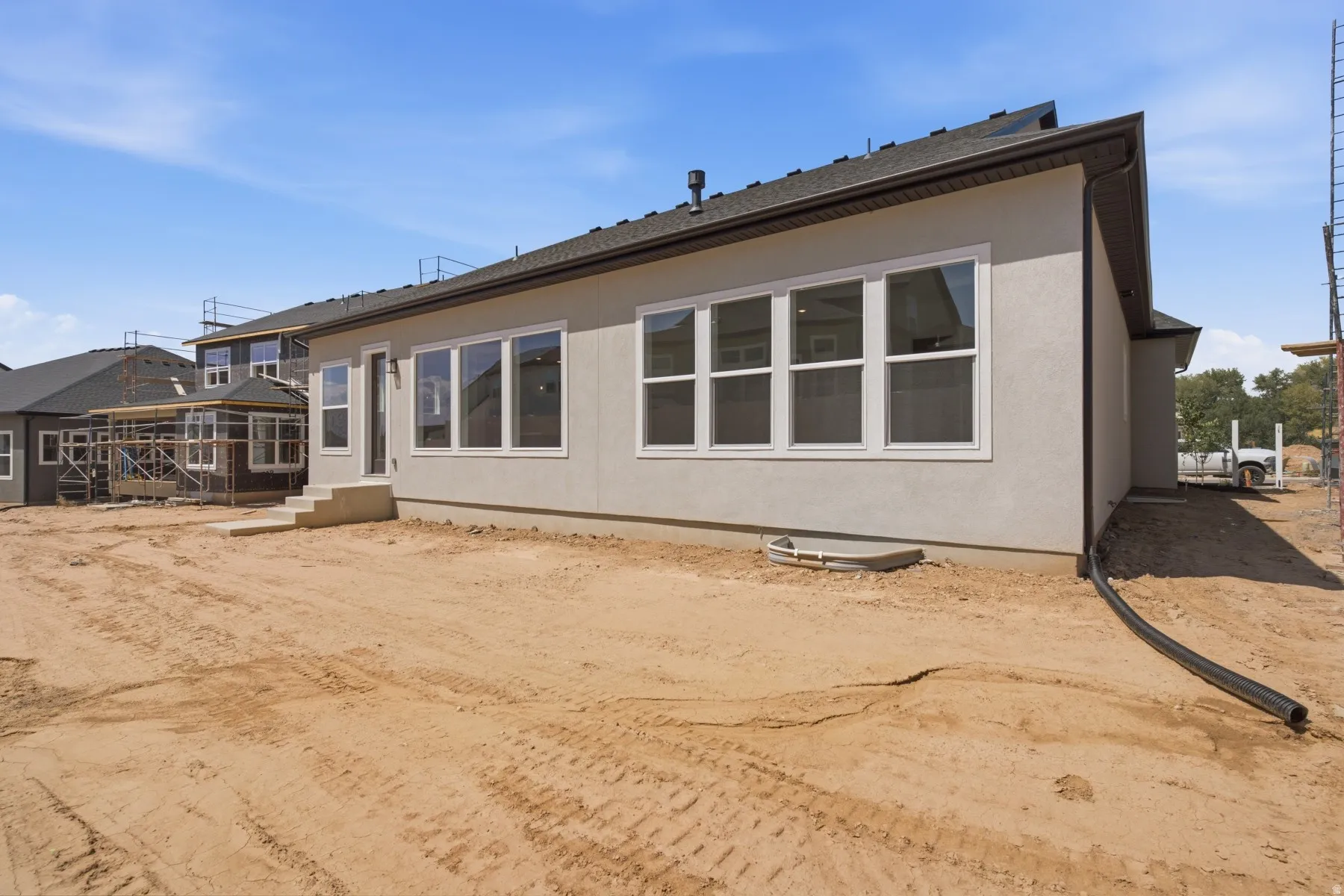 Light-toned stucco exterior with multiple windows, a dark shingle roof, and a concrete patio