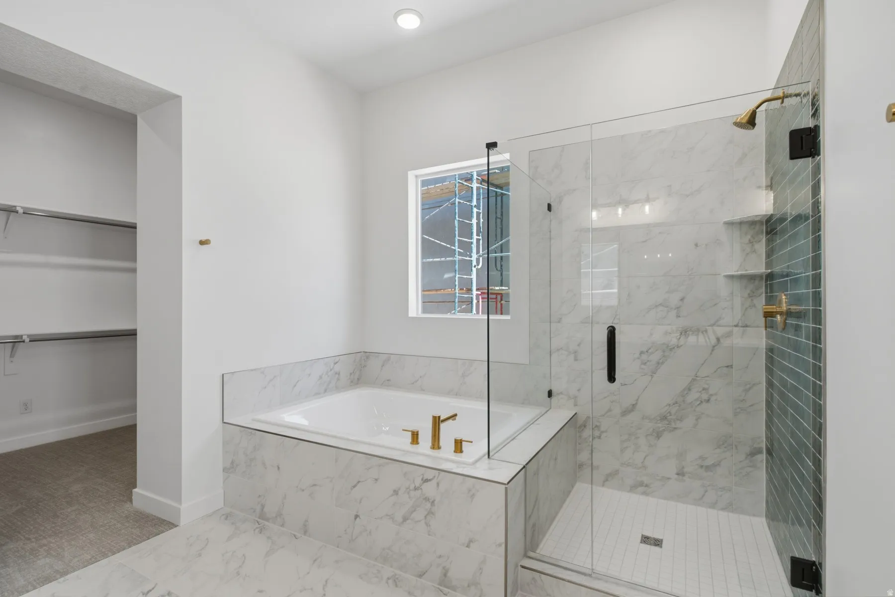 Soaking tub with gold-tone fixtures, glass-enclosed shower with tile surround, and marble-look wall and floor tiling