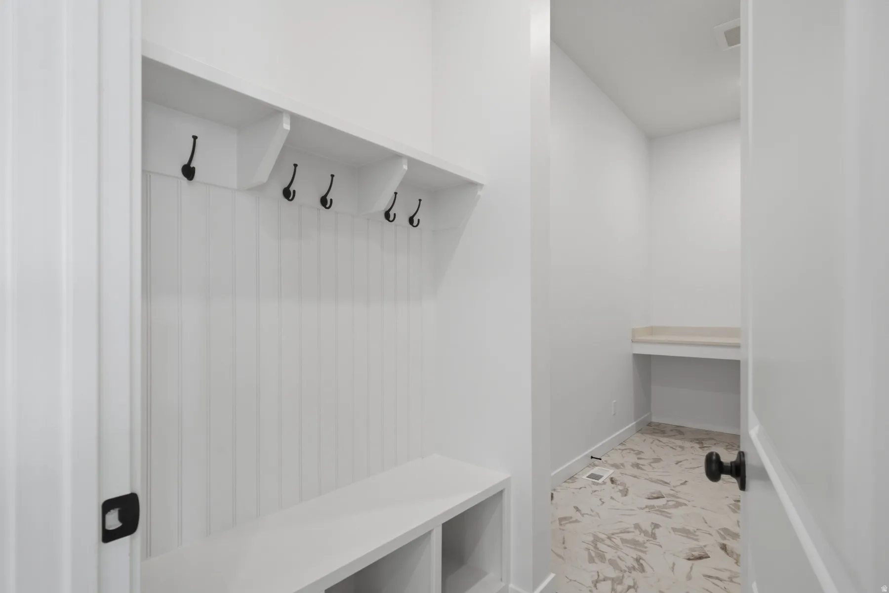 Built-in white storage bench with open shelving, beadboard backing, and black hooks