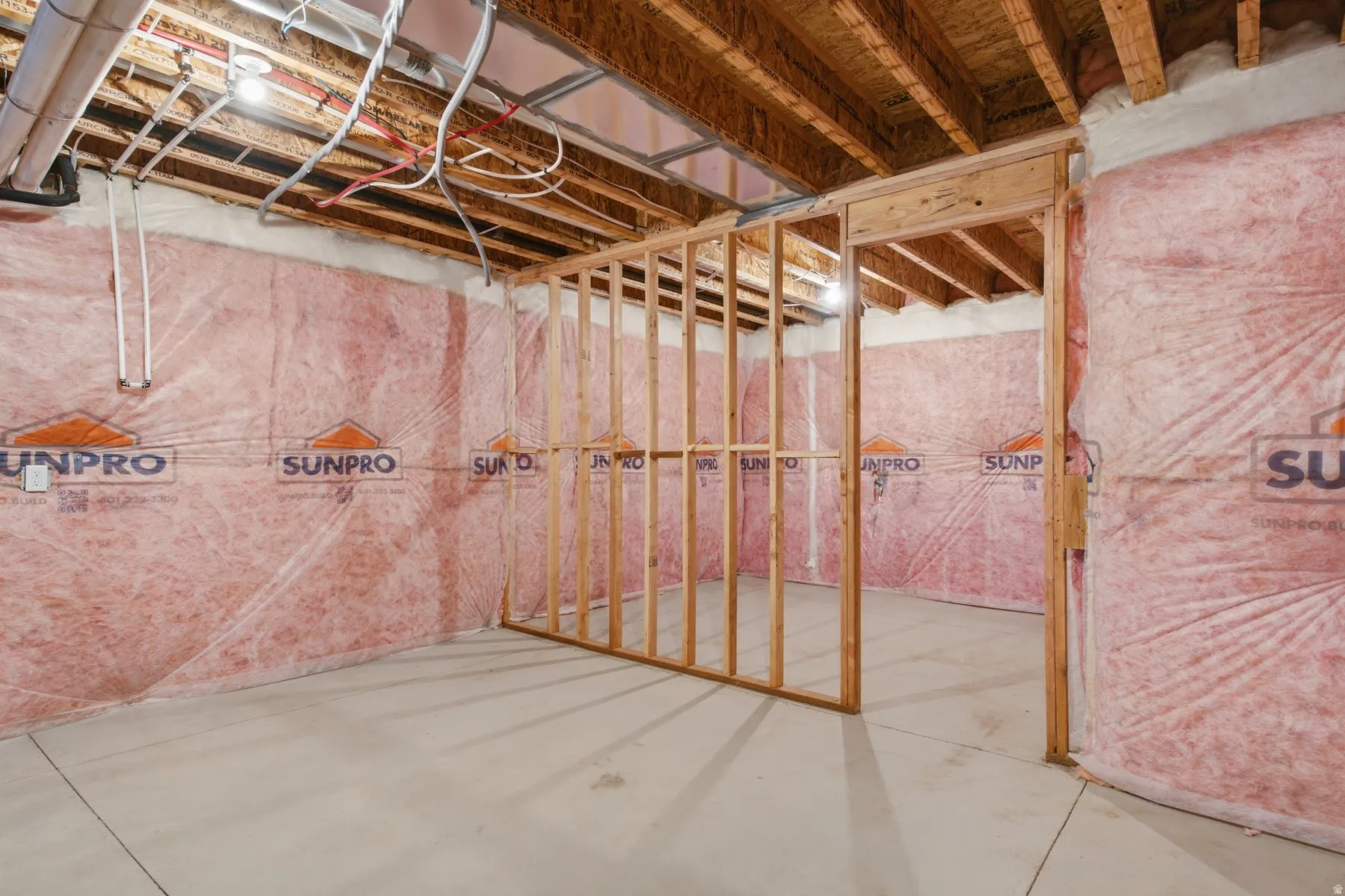 Unfinished lower level with concrete flooring, exposed wood ceiling joists, and insulated walls