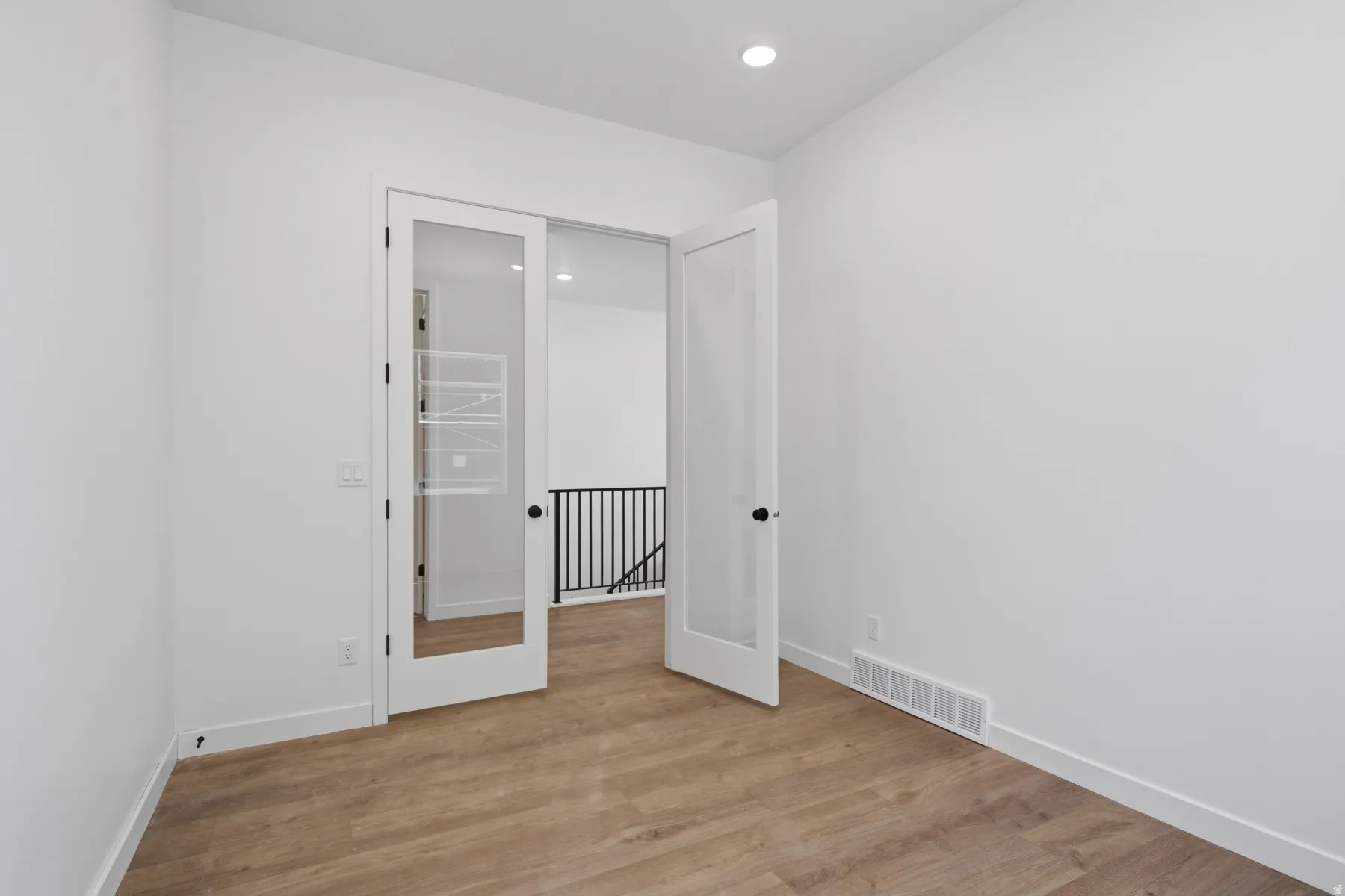 Wood-finish flooring, recessed ceiling lighting, and French doors with privacy glass
