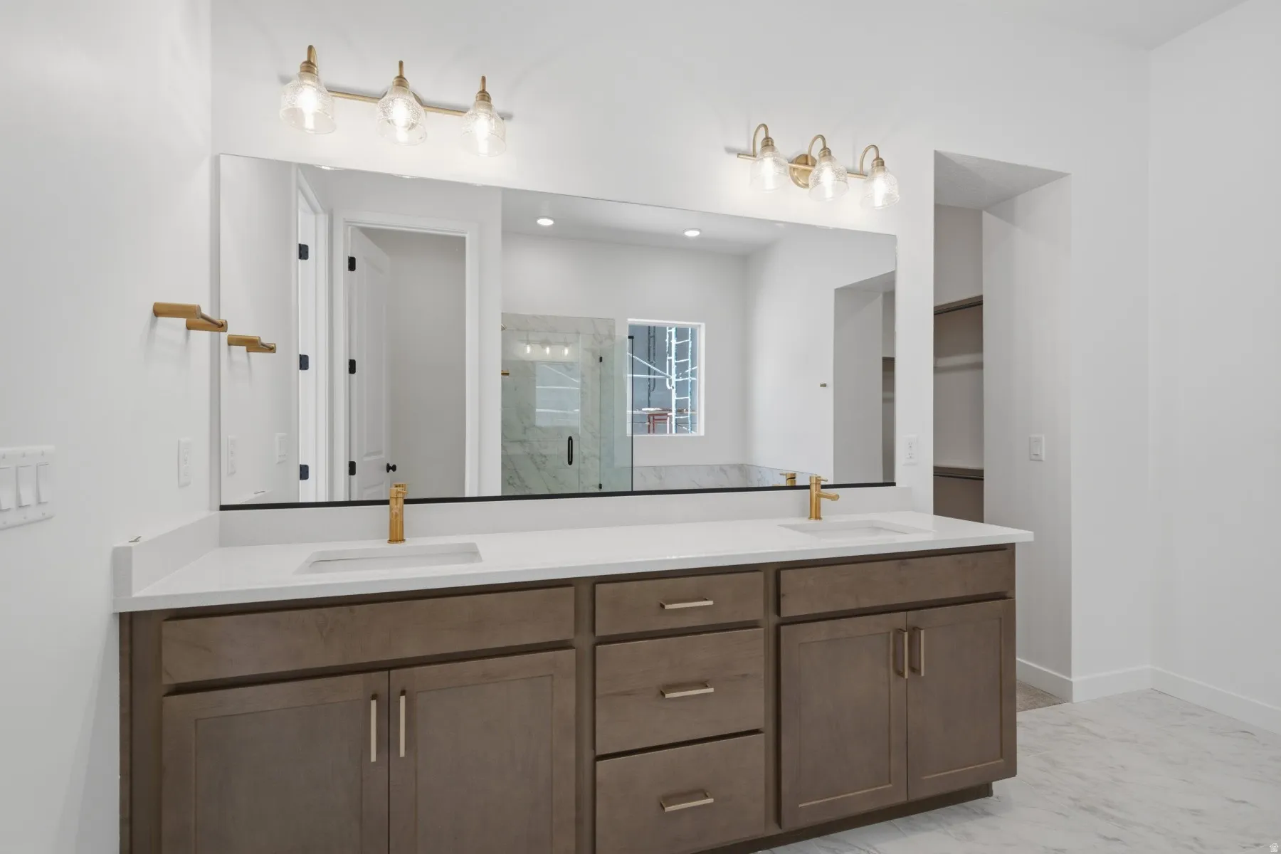 Dual vanity with integrated sinks, brushed brass fixtures, white countertops, and wood-finish cabinetry