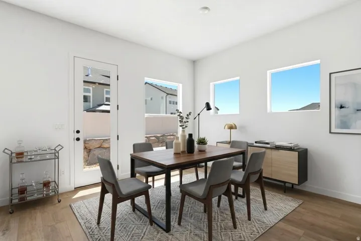 Contemporary dining space featuring a wood-finish table with metal frame seating for four, wide-plank wood flooring, and abundant natural light from multiple windows