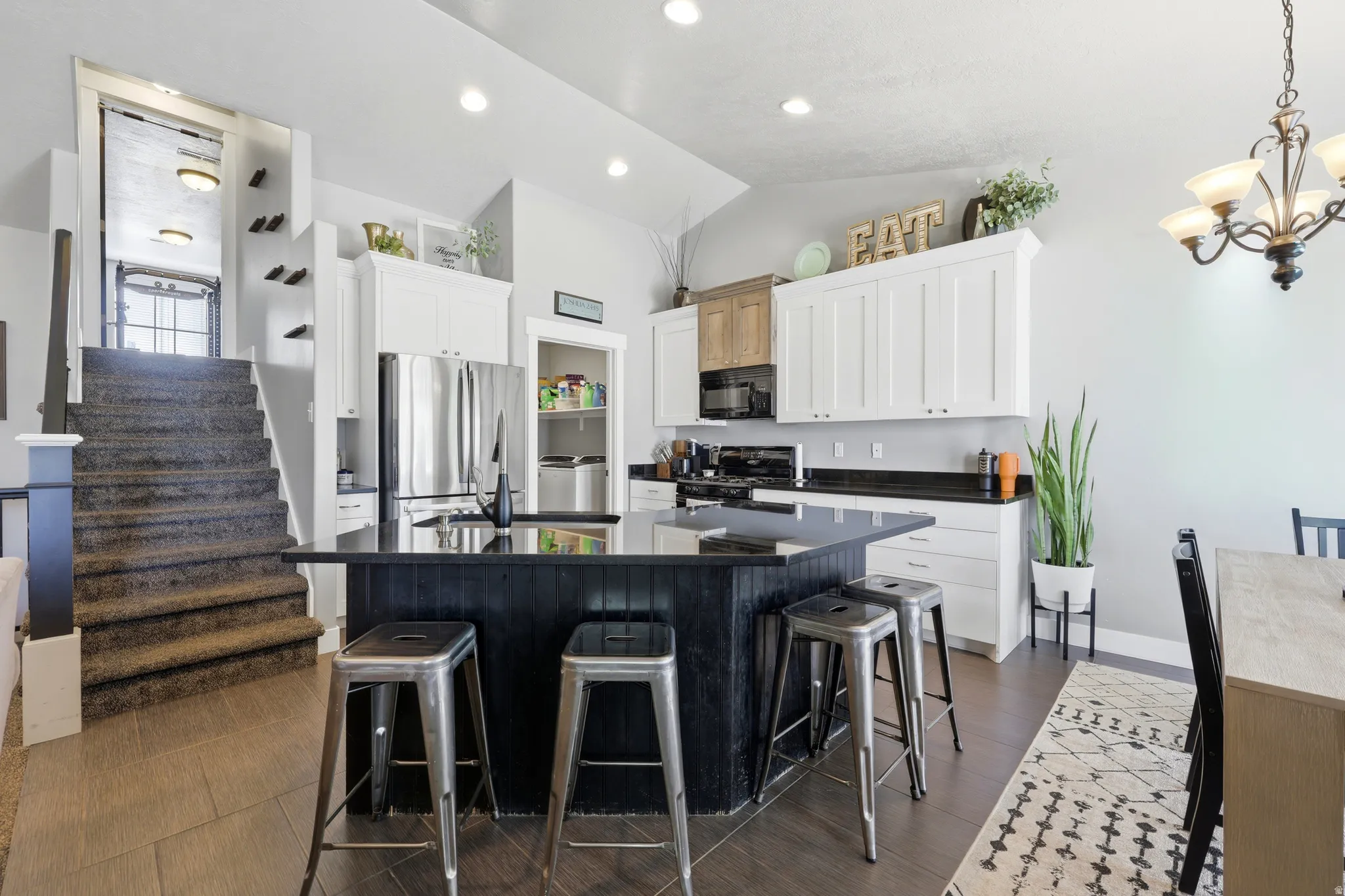 Kitchen featuring a large island with black paneling, white shaker-style cabinetry, dark countertops, and stainless steel appliances