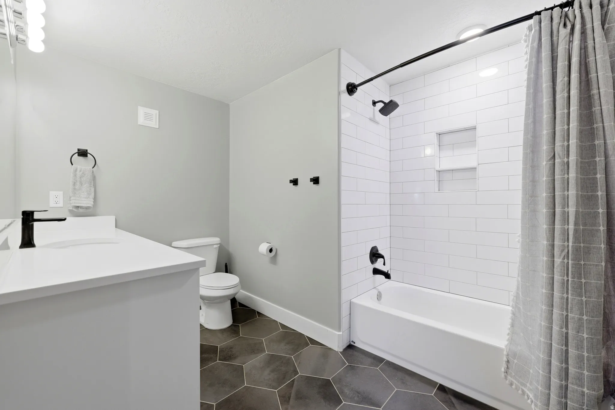 Bathroom featuring a white vanity with integrated sink, black fixtures, hexagon tile flooring, and a subway-tiled shower with recessed shelving