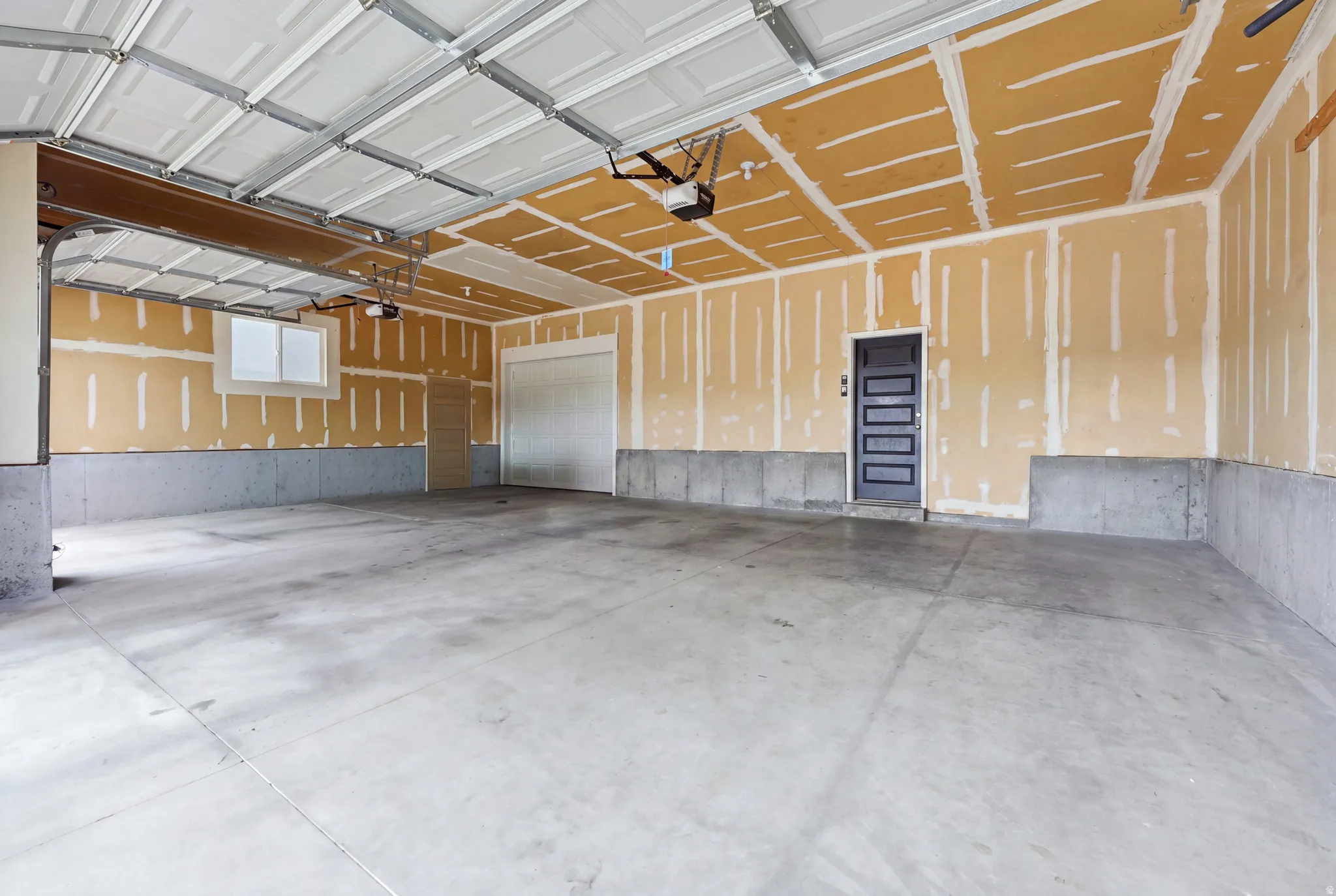 Spacious garage with concrete flooring, two overhead garage doors, an internal access door, a secondary side door, and a window for natural light