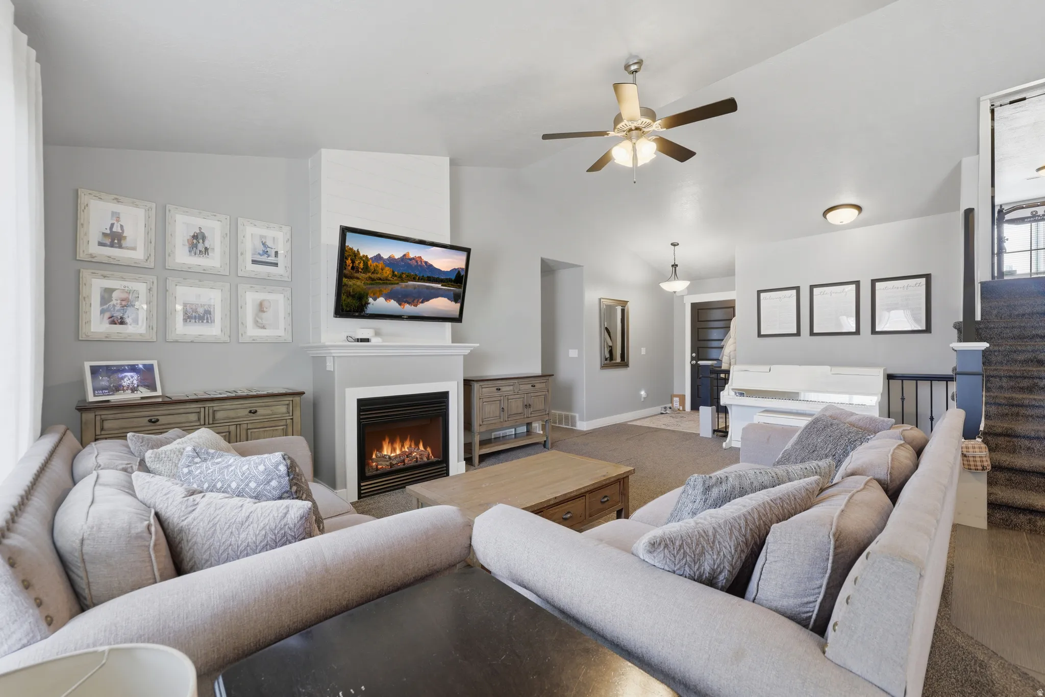 Living area featuring a ceiling fan, a fireplace with a white mantel, and a dark-toned door